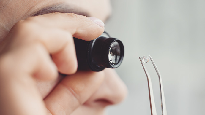 Woman looks through magnifying glass at precious stone. Stone authentication concept