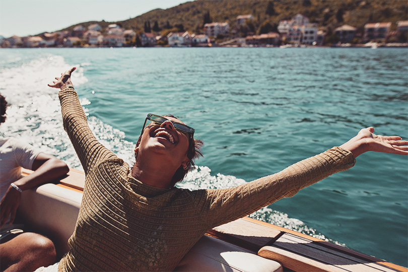 Happy young woman with arms raised in motorboat enjoying sunny day