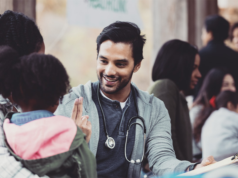 Volunteer doctor holds up two fingers as he checks a young girl's vision. The girl and her mom are visiting an outdoor free clinic.