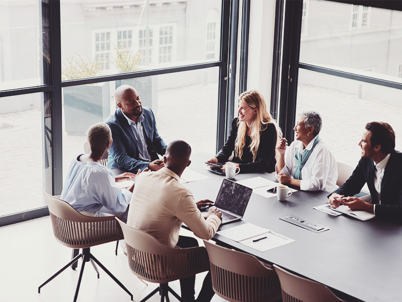 Smiling group of diverse businesspeople talking together around a conference table during a boardroom meeting in a modern office