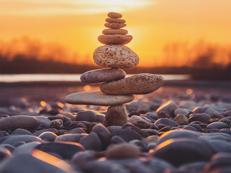 Close-up of stacked pebbles at beach against sky during sunset